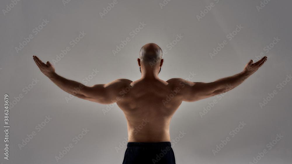 Perfect shape. Rear view of muscular strong man with naked torso standing with outstretched arms isolated over grey background