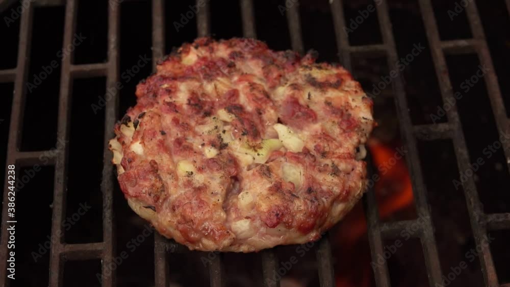 A chief is rotating delicious homemade meat cutlet for a burger on the grill grid with a wooden fork A chief is rotating delicious homemade meat cutlet for a burger on the grill grid with a wooden fork