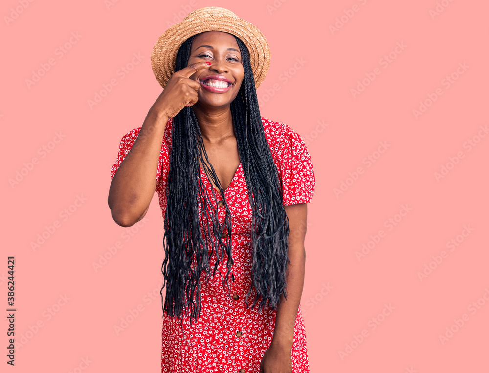 Young african american woman wearing summer hat pointing with hand finger to face and nose, smiling cheerful. beauty concept Young african american woman wearing summer hat pointing with hand finger to face and nose, smiling cheerful. beauty concept