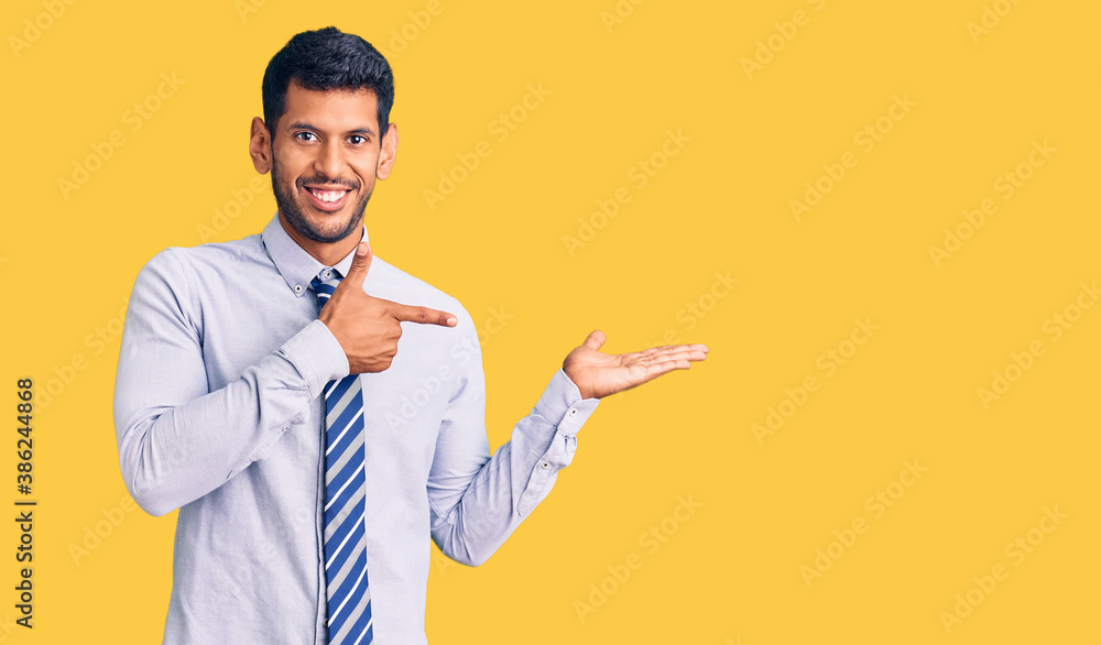 Young latin man wearing business clothes amazed and smiling to the camera while presenting with hand and pointing with finger. Young latin man wearing business clothes amazed and smiling to the camera while presenting with hand and pointing with finger.