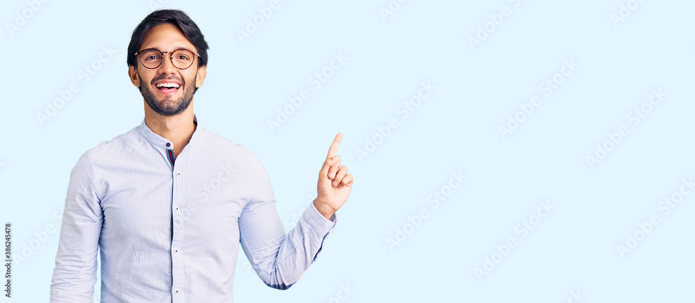 Handsome hispanic man wearing business shirt and glasses with a big smile on face, pointing with hand finger to the side looking at the camera. Handsome hispanic man wearing business shirt and glasses with a big smile on face, pointing with hand finger to the side looking at the camera.