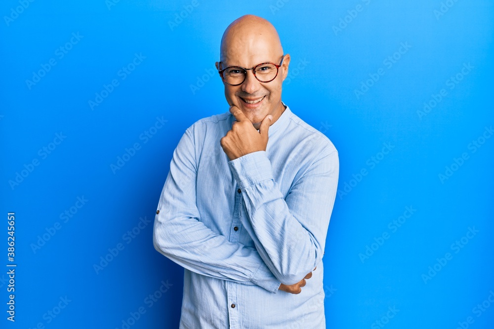 Middle age bald man wearing casual clothes and glasses looking confident at the camera smiling with crossed arms and hand raised on chin. thinking positive. Middle age bald man wearing casual clothes and glasses looking confident at the camera smiling with crossed arms and hand raised on chin. thinking positive.
