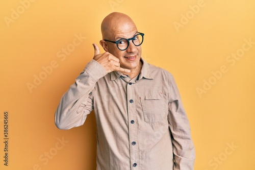 Middle age bald man wearing casual clothes and glasses smiling doing phone gesture with hand and fingers like talking on the telephone. communicating concepts. © Krakenimages.com