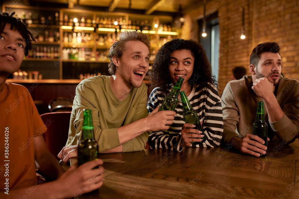 Friends in the bar watching sports match on TV together, drinking beer, clinking bottles and cheering for team. People, leisure, friendship and entertainment concept