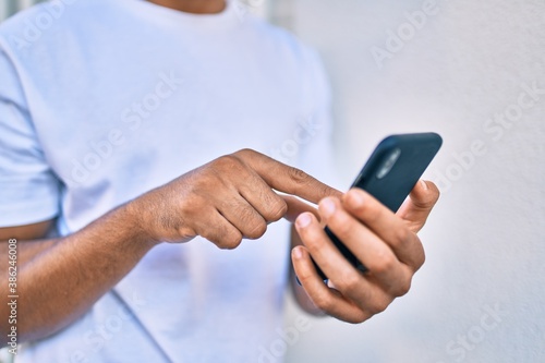 Young arab man smiling happy using smartphone leaning on the wall.