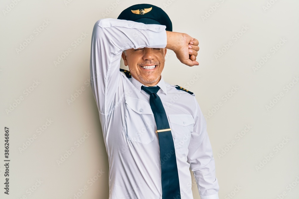 Handsome middle age mature man wearing airplane pilot uniform covering eyes with arm smiling cheerful and funny. blind concept.