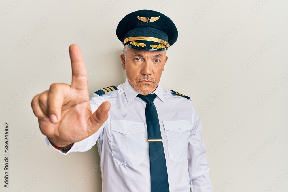 Handsome middle age mature man wearing airplane pilot uniform pointing with finger up and angry expression, showing no gesture
