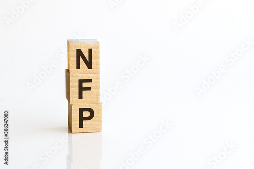 Three wooden cubes with letters NFP - Nonfarm payrolls, on white table, more in background, space for text in right down corner photo