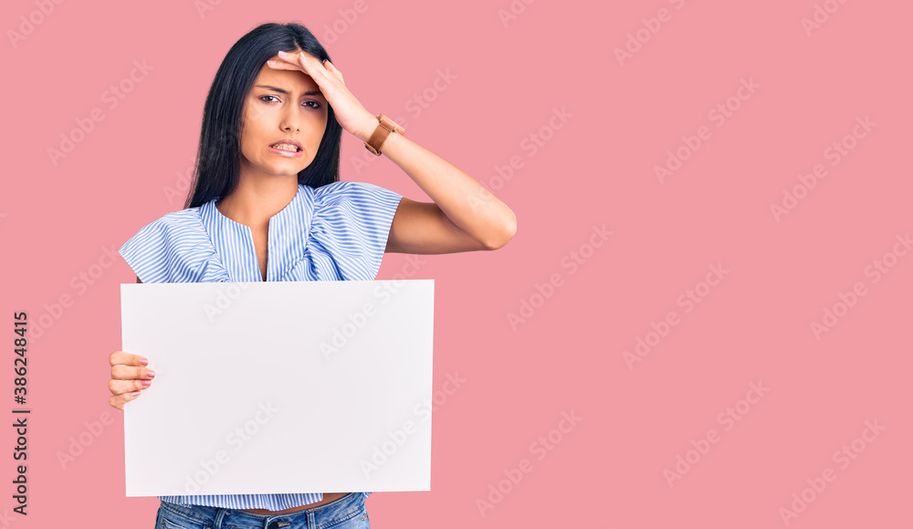 Young beautiful latin girl holding blank empty banner stressed and frustrated with hand on head, surprised and angry face Young beautiful latin girl holding blank empty banner stressed and frustrated with hand on head, surprised and angry face