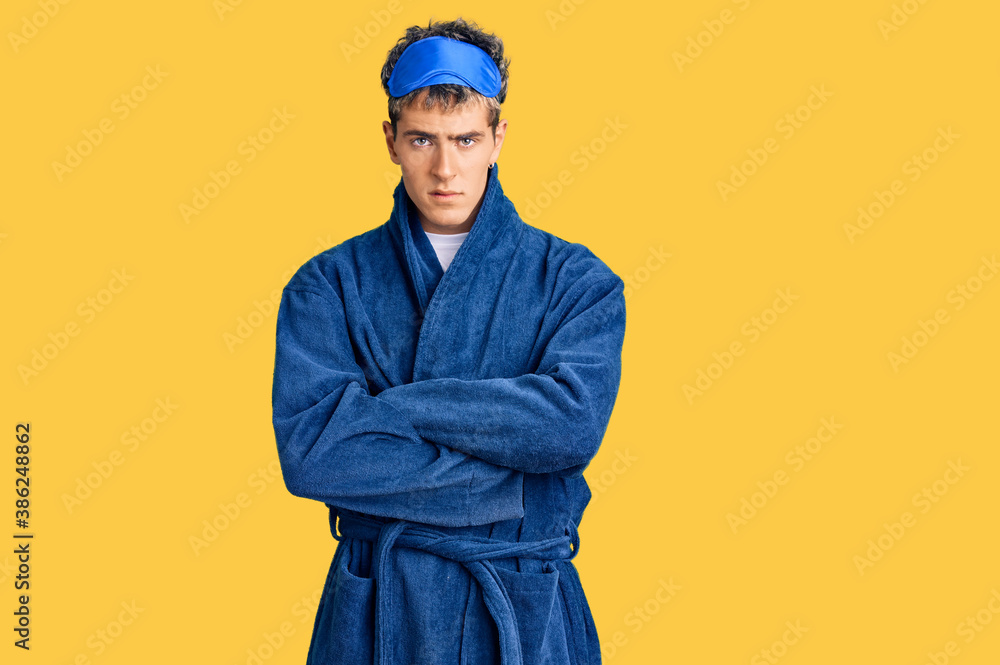 Young handsome man wearing sleep mask and bathrobe skeptic and nervous, disapproving expression on face with crossed arms. negative person.