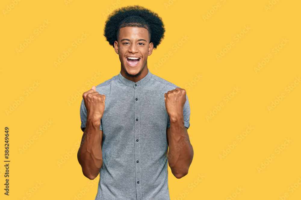 African american man with afro hair wearing casual clothes celebrating surprised and amazed for success with arms raised and open eyes. winner concept. African american man with afro hair wearing casual clothes celebrating surprised and amazed for success with arms raised and open eyes. winner concept.