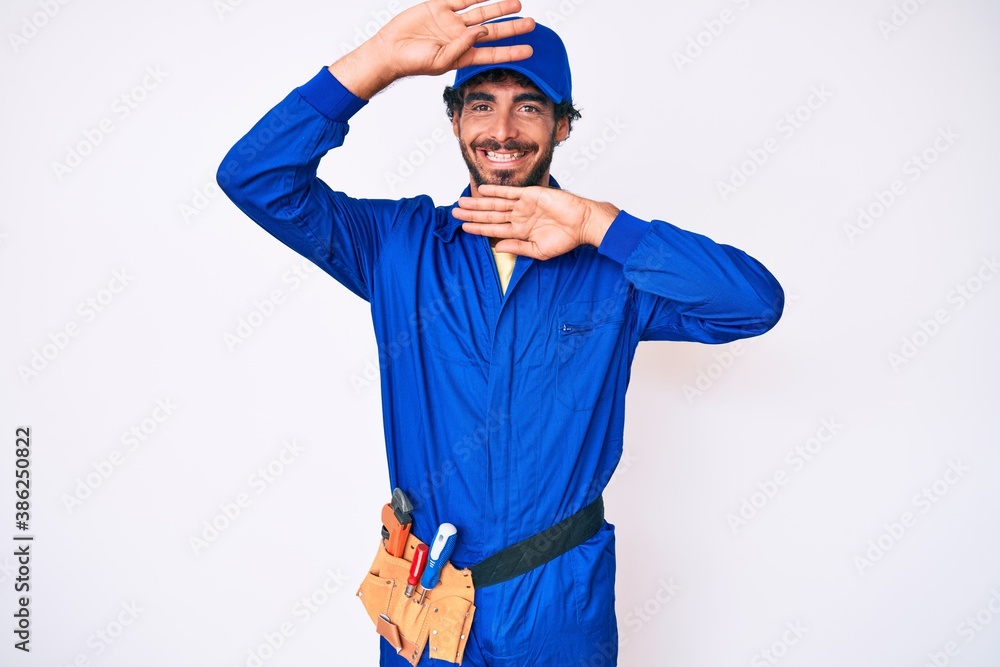 Handsome young man with curly hair and bear weaing handyman uniform smiling cheerful playing peek a boo with hands showing face. surprised and exited Handsome young man with curly hair and bear weaing handyman uniform smiling cheerful playing peek a boo with hands showing face. surprised and exited