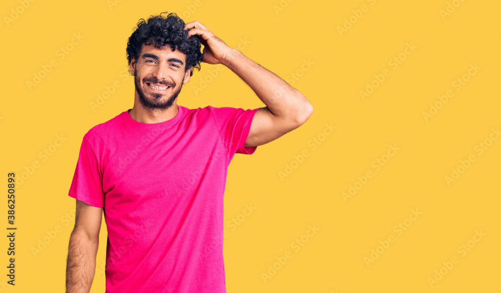 Handsome young man with curly hair and bear wearing casual pink tshirt confuse and wonder about question. uncertain with doubt, thinking with hand on head. pensive concept. Handsome young man with curly hair and bear wearing casual pink tshirt confuse and wonder about question. uncertain with doubt, thinking with hand on head. pensive concept.
