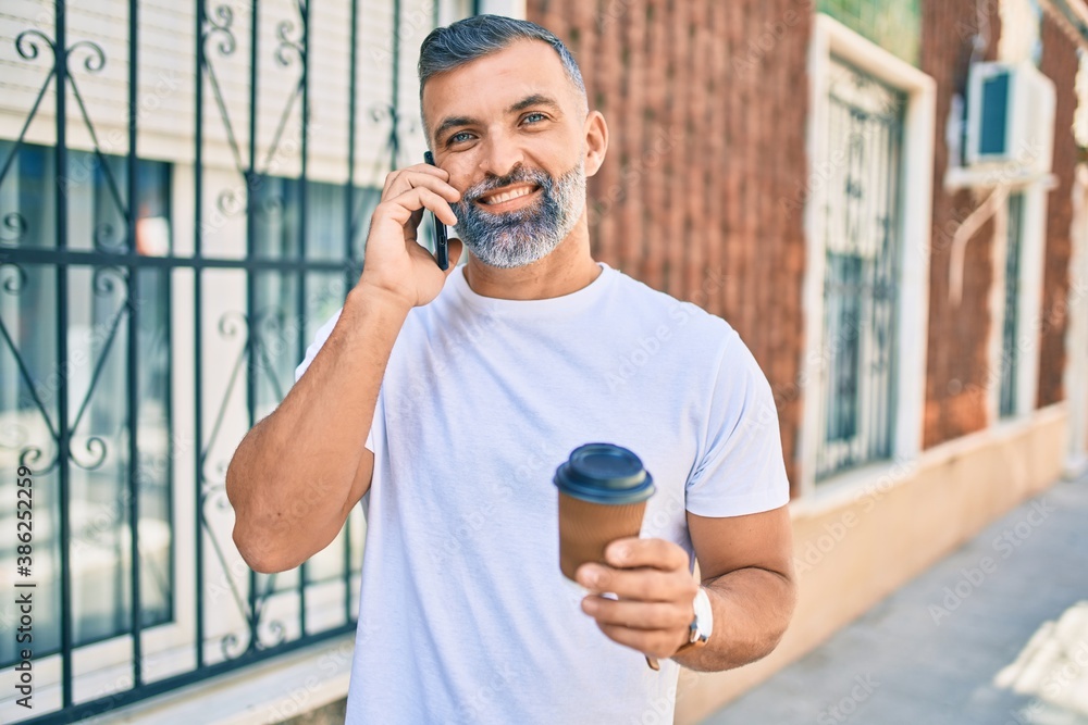 Middle age grey-haired man talking on the smartphone and drinking take away coffee at the city Middle age grey-haired man talking on the smartphone and drinking take away coffee at the city