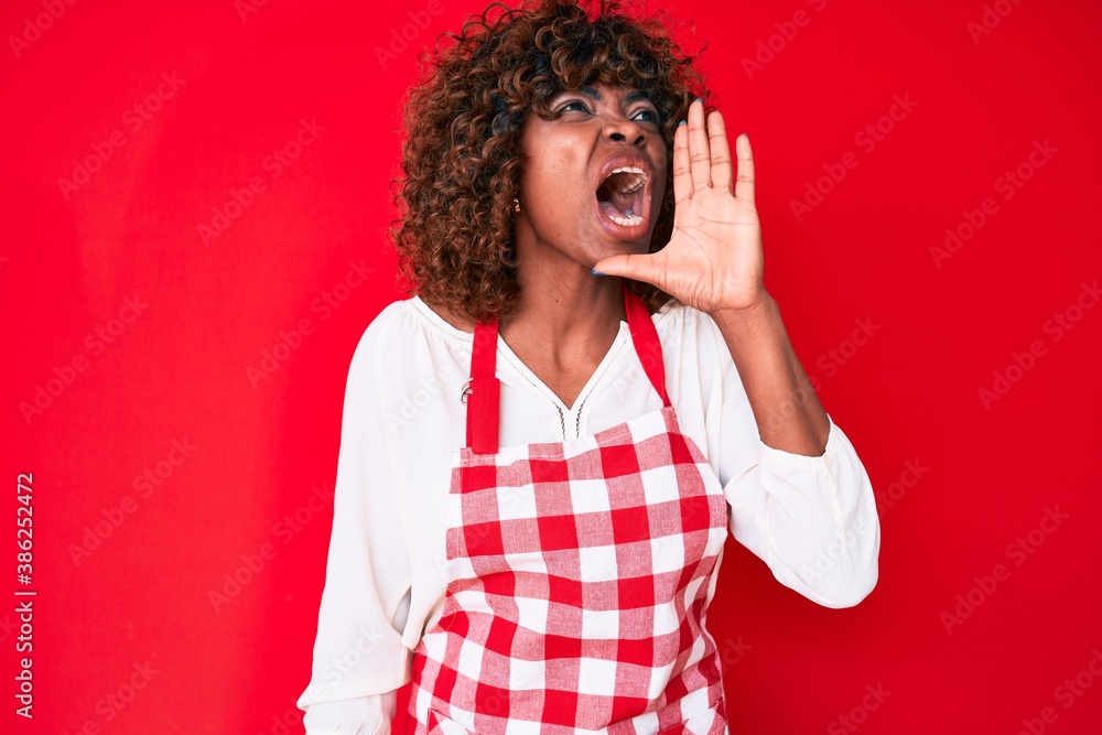 Young african american woman wearing apron shouting and screaming loud to side with hand on mouth. communication concept. Young african american woman wearing apron shouting and screaming loud to side with hand on mouth. communication concept.