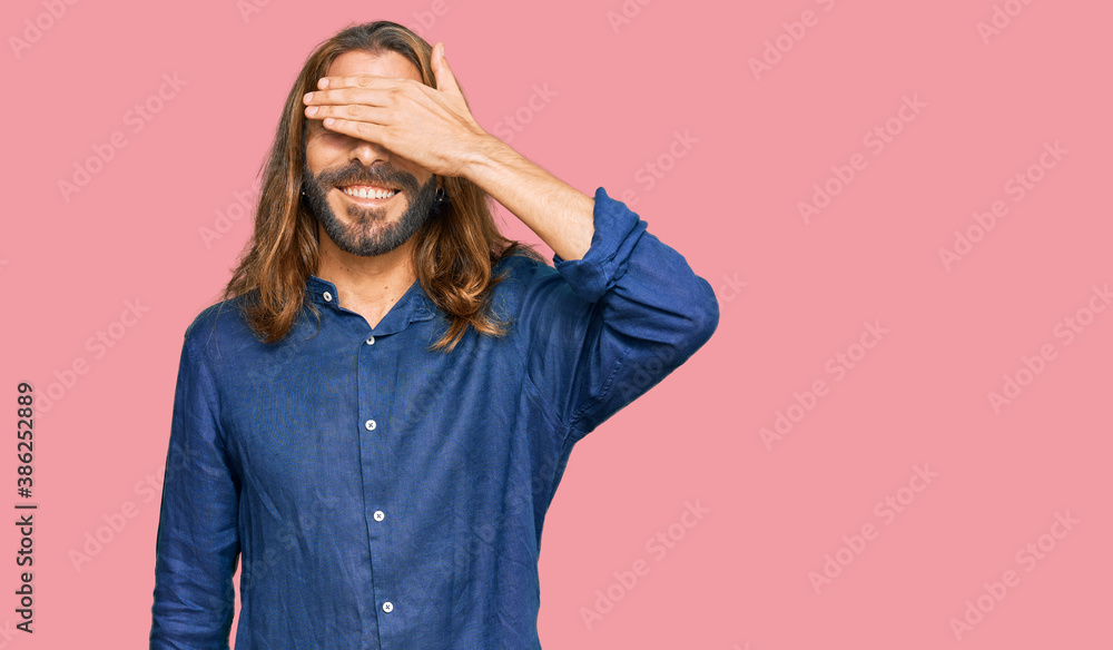 Attractive man with long hair and beard wearing casual clothes smiling and laughing with hand on face covering eyes for surprise. blind concept. Attractive man with long hair and beard wearing casual clothes smiling and laughing with hand on face covering eyes for surprise. blind concept.