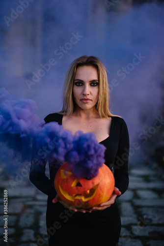 A young witch holds a steaming pumpkin with a terrible face in her hands. Halloween concept.