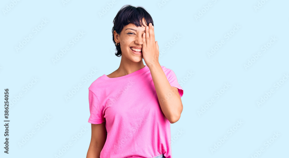 Young brunette woman with short hair wearing casual clothes covering one eye with hand, confident smile on face and surprise emotion. Young brunette woman with short hair wearing casual clothes covering one eye with hand, confident smile on face and surprise emotion.