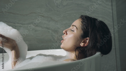 Attractive woman bathing indoors. Cute girl having fun with foam in bathroom. photo