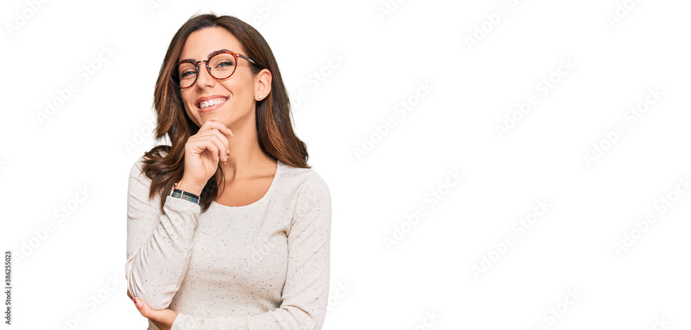 Young brunette woman wearing casual clothes and glasses looking confident at the camera with smile with crossed arms and hand raised on chin. thinking positive. Young brunette woman wearing casual clothes and glasses looking confident at the camera with smile with crossed arms and hand raised on chin. thinking positive.