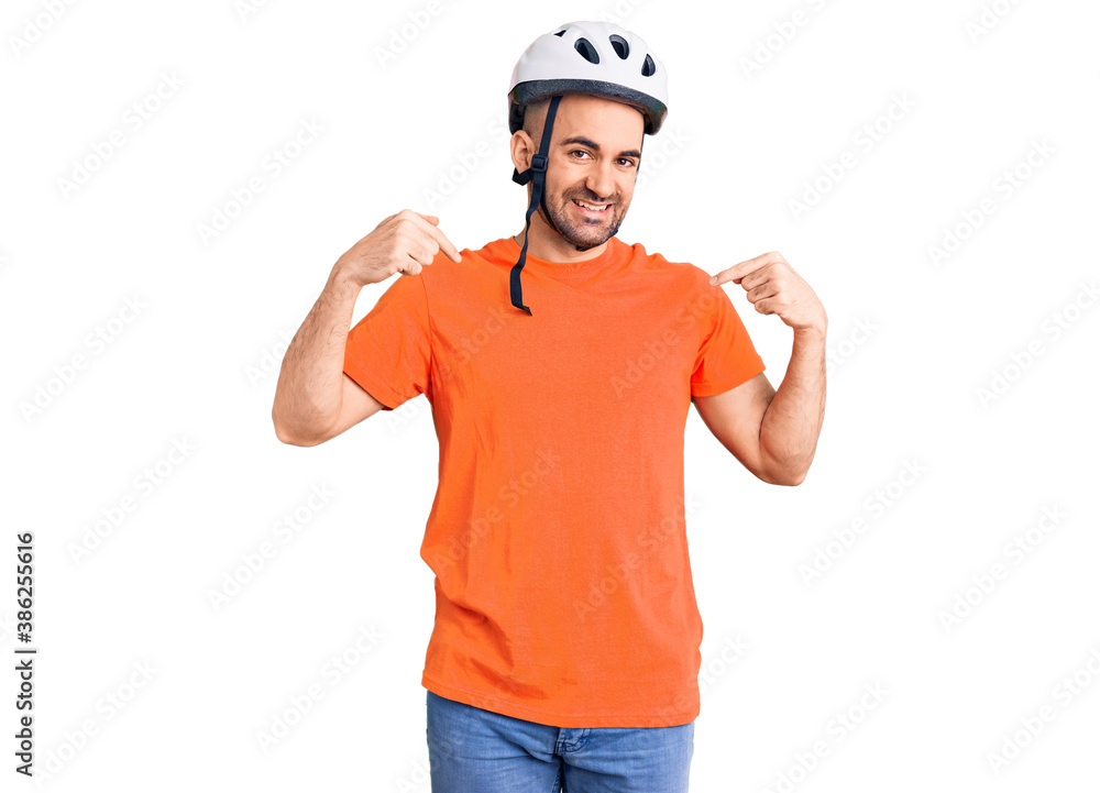 Young handsome man wearing bike helmet looking confident with smile on face, pointing oneself with fingers proud and happy.