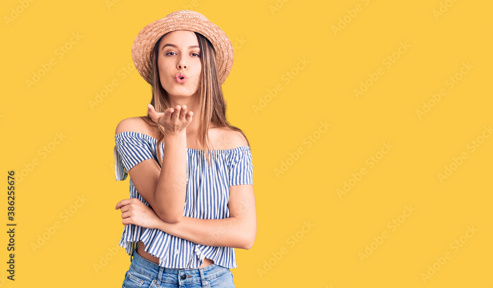 Young beautiful girl wearing hat and t shirt looking at the camera blowing a kiss with hand on air being lovely and sexy. love expression. Young beautiful girl wearing hat and t shirt looking at the camera blowing a kiss with hand on air being lovely and sexy. love expression.