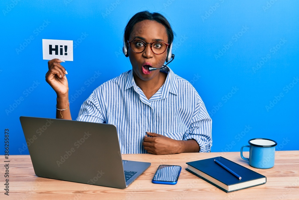 Young african woman wearing operator headset holding hi word scared and amazed with open mouth for surprise, disbelief face Young african woman wearing operator headset holding hi word scared and amazed with open mouth for surprise, disbelief face