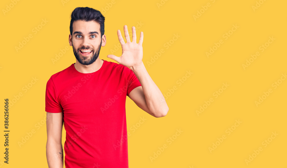 Young handsome man with beard wearing casual t-shirt showing and pointing up with fingers number five while smiling confident and happy. Young handsome man with beard wearing casual t-shirt showing and pointing up with fingers number five while smiling confident and happy.