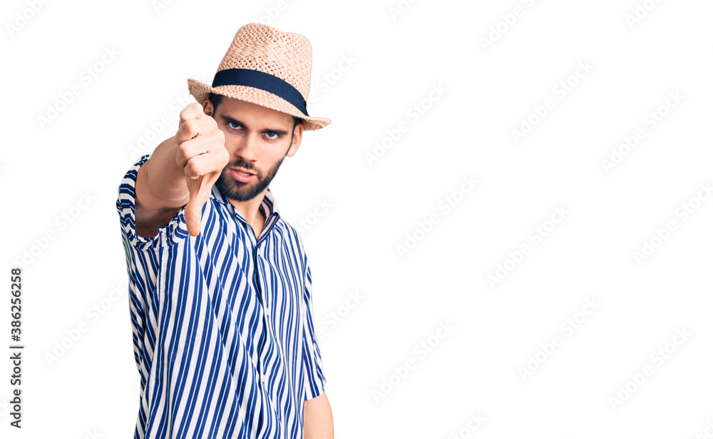 Young handsome man with beard wearing summer hat and striped shirt looking unhappy and angry showing rejection and negative with thumbs down gesture. bad expression. Young handsome man with beard wearing summer hat and striped shirt looking unhappy and angry showing rejection and negative with thumbs down gesture. bad expression.