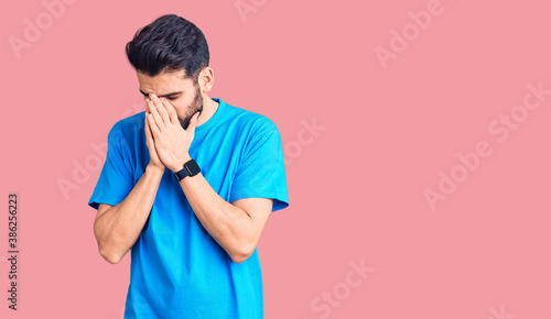 Young handsome man with beard wearing casual t-shirt with sad expression covering face with hands while crying. depression concept.