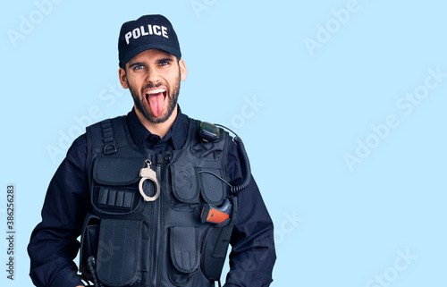 Young handsome man with beard wearing police uniform sticking tongue out happy with funny expression. emotion concept.