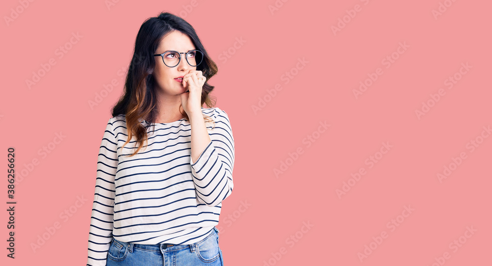 Beautiful young brunette woman wearing casual clothes and glasses looking stressed and nervous with hands on mouth biting nails. anxiety problem. Beautiful young brunette woman wearing casual clothes and glasses looking stressed and nervous with hands on mouth biting nails. anxiety problem.