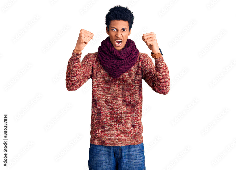 Young african american man wearing casual winter sweater and scarf angry and mad raising fists frustrated and furious while shouting with anger. rage and aggressive concept. Young african american man wearing casual winter sweater and scarf angry and mad raising fists frustrated and furious while shouting with anger. rage and aggressive concept.