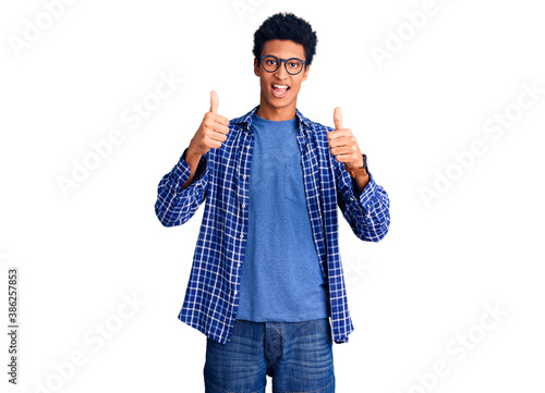 Young african american man wearing casual clothes and glasses success sign doing positive gesture with hand, thumbs up smiling and happy. cheerful expression and winner gesture.