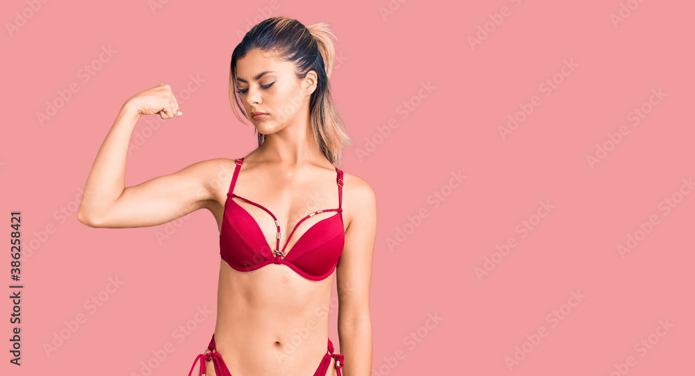 Fototapeta premium Young beautiful woman wearing bikini strong person showing arm muscle, confident and proud of power