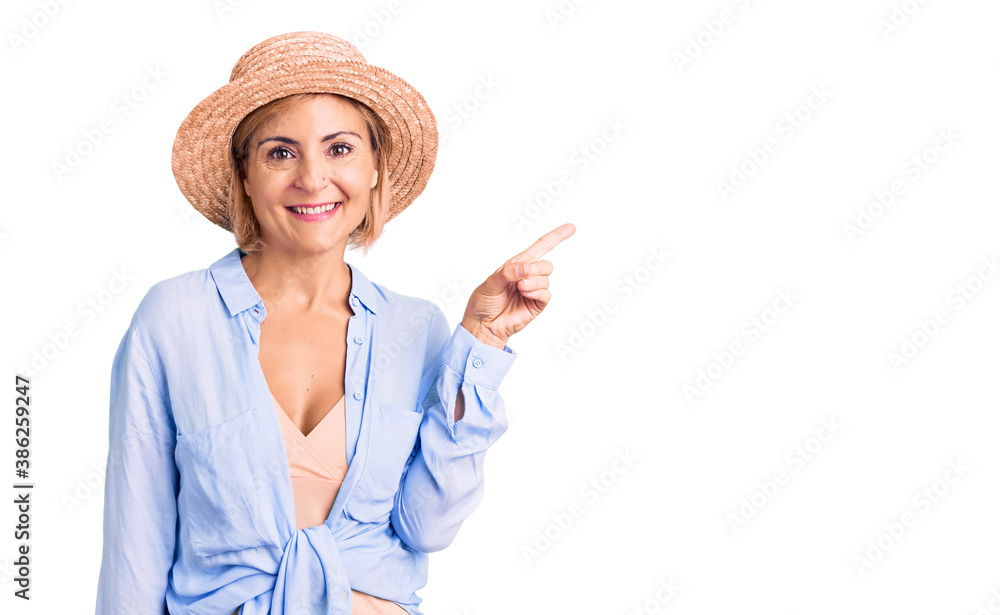 Young blonde woman wearing summer hat smiling happy pointing with hand and finger to the side Young blonde woman wearing summer hat smiling happy pointing with hand and finger to the side