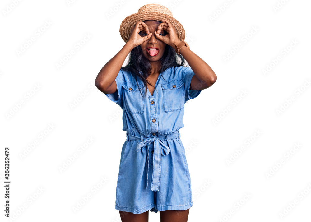 Young indian girl wearing summer hat doing ok gesture like binoculars sticking tongue out, eyes looking through fingers. crazy expression. Young indian girl wearing summer hat doing ok gesture like binoculars sticking tongue out, eyes looking through fingers. crazy expression.