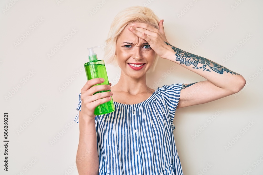 Young blonde woman with tattoo holding aloe vera stressed and frustrated with hand on head, surprised and angry face Young blonde woman with tattoo holding aloe vera stressed and frustrated with hand on head, surprised and angry face