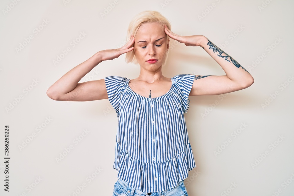 Young blonde woman with tattoo wearing casual clothes with hand on head, headache because stress. suffering migraine. Young blonde woman with tattoo wearing casual clothes with hand on head, headache because stress. suffering migraine.