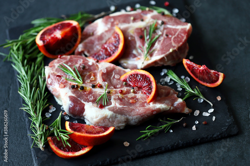 Selective focus. Macro. Raw pork steaks with rosemary and orange marinated on a stone board. Cooking meat steaks.