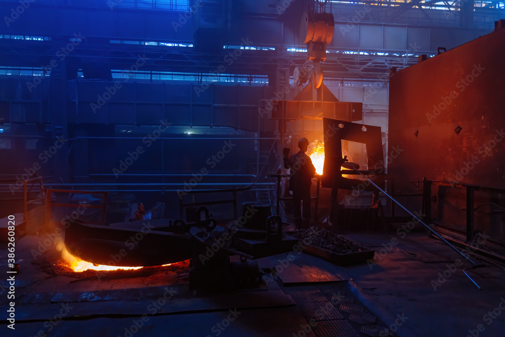 Worker operates metal casting process in metallurgical plant