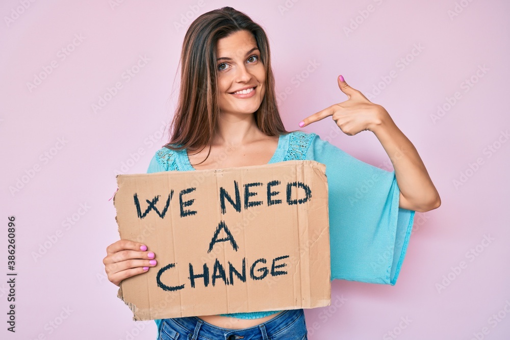 Beautiful caucasian woman holding we need a change banner pointing finger to one self smiling happy and proud Beautiful caucasian woman holding we need a change banner pointing finger to one self smiling happy and proud