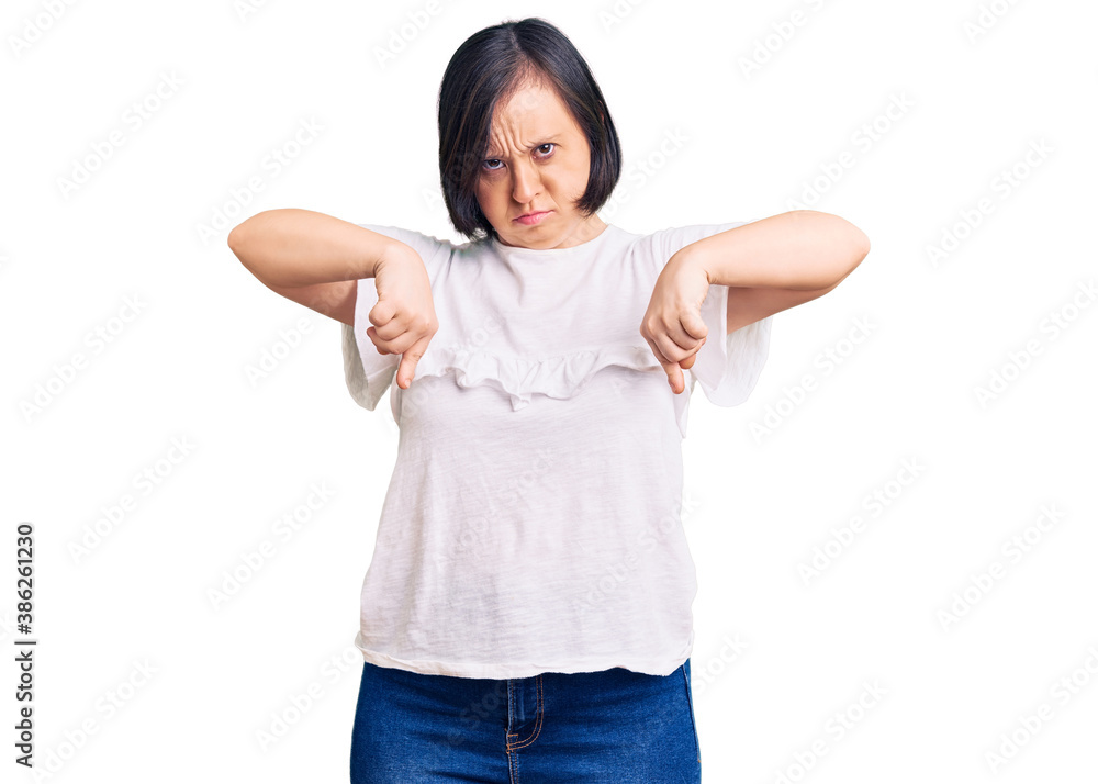 Brunette woman with down syndrome wearing casual white tshirt pointing down looking sad and upset, indicating direction with fingers, unhappy and depressed. Brunette woman with down syndrome wearing casual white tshirt pointing down looking sad and upset, indicating direction with fingers, unhappy and depressed.
