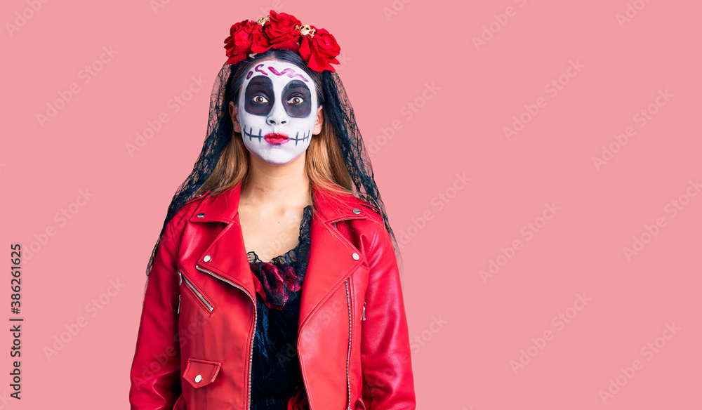 Woman wearing day of the dead costume over background puffing cheeks with funny face. mouth inflated with air, crazy expression. Woman wearing day of the dead costume over background puffing cheeks with funny face. mouth inflated with air, crazy expression.