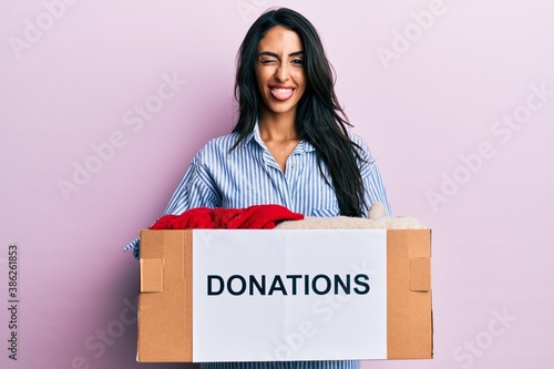 Beautiful hispanic woman volunteer holding donations box sticking tongue out happy with funny expression. © Krakenimages.com