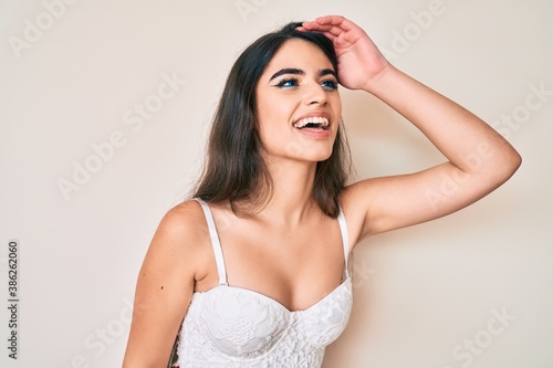 Brunette teenager girl posing elegant very happy and smiling looking far away with hand over head. searching concept.