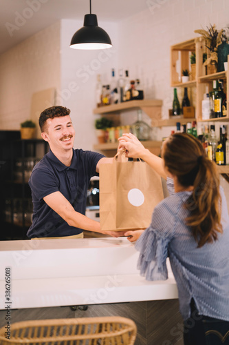 Portrait of a professional waiter handing to a customer a takeaway order in a recycled paper bag at the restaurant.