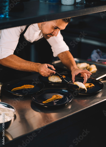 Portrait  of a male chef serving fried cod in ceramic blue dish over stainless steel worktop in restaurant kitchen.