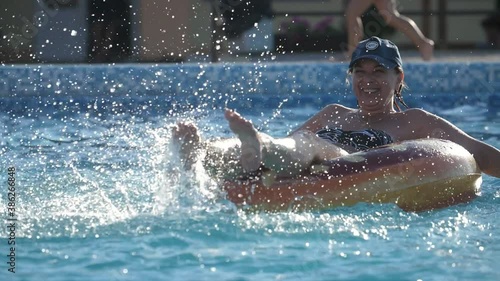 Happy woman sitting on a water dounut dabbling her legs in a pool in slow motion photo