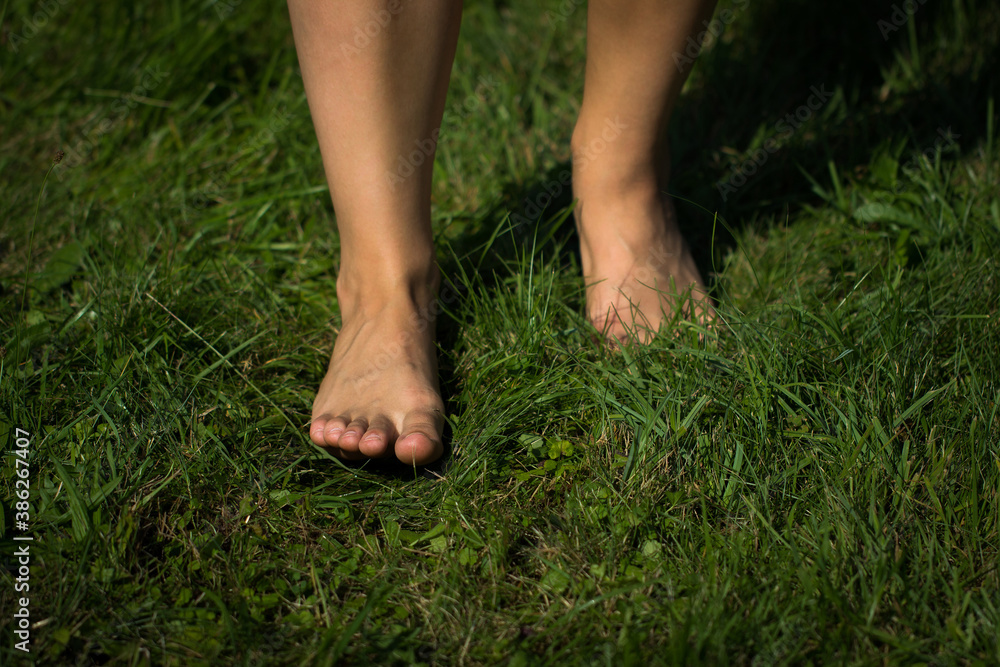 Woman's barefoot walking on the fresh, green grass in the sunny morning. Healthy lifestyle.
